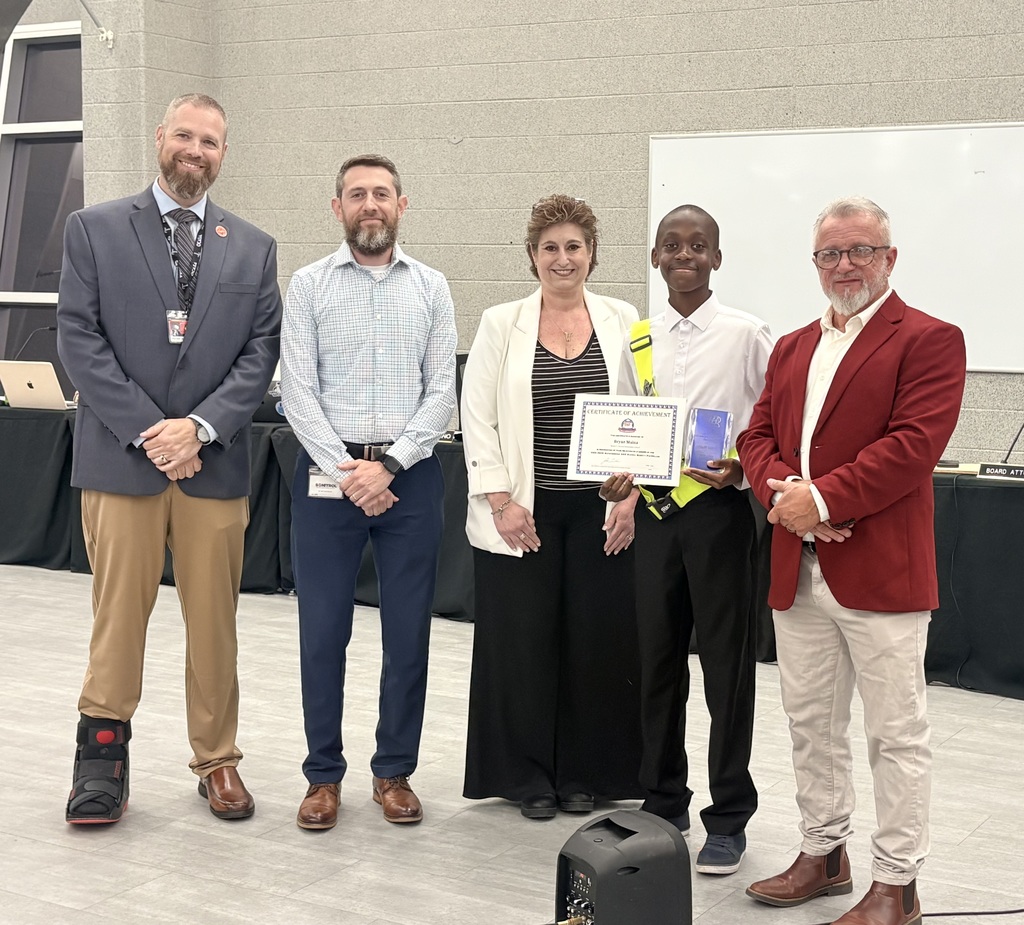 Image of Bryan holding his award and certificate posing with the Superintendent, BOE President, teacher, and the AAA Club Alliance representative. 