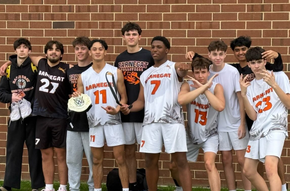 Image of the boys' volleyball team posing together outside of a brick school wall after their win. 