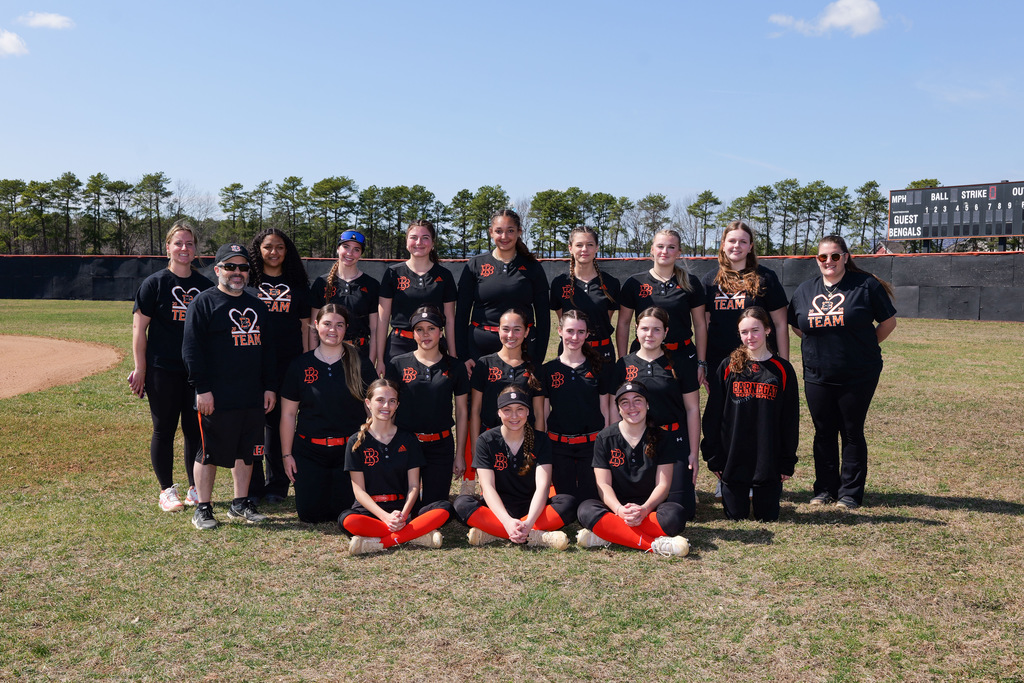 Image of the girls varsity softball team posing on the field with their coaches. 