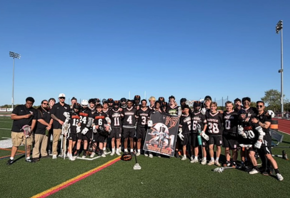 Image of the boys lacrosse team surrounding Cedryk while he holds a sign as the new school record holder.  