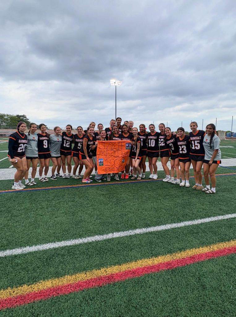 Image of the girls lacrosse team posing with Lizzie on the flied holding a sign for celebration. 
