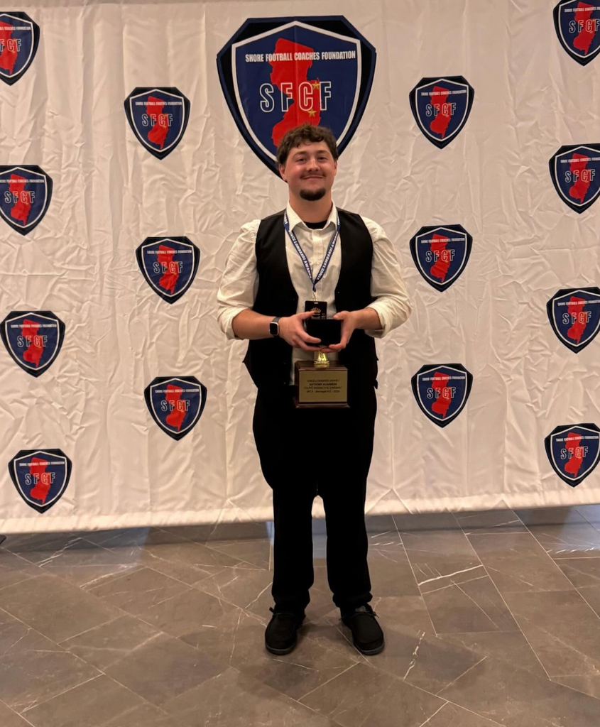 Image of Anthony posing in front of the SFCF wall banner holding his trophy. 