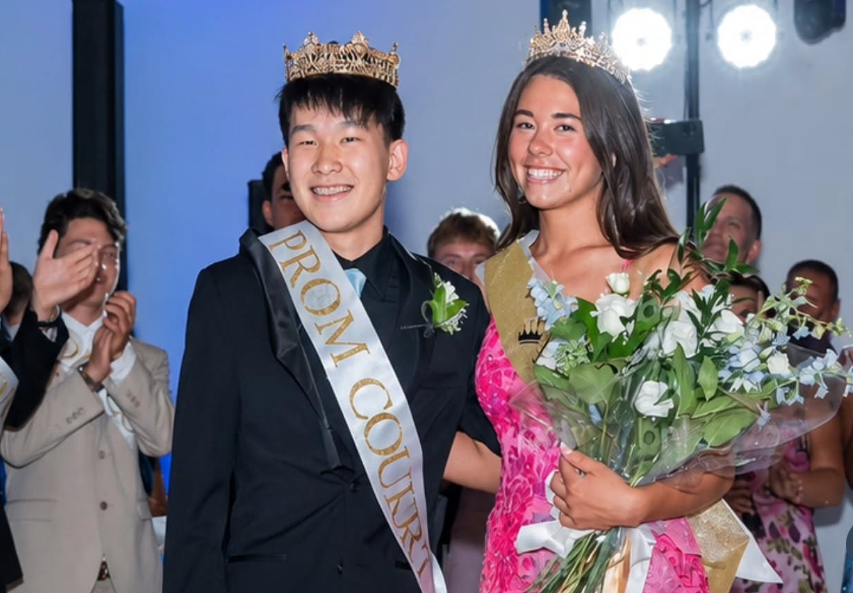 Image of Devin and Emma posing together wearing their crowns and prom court sashes while Emma holds a bouquet of flowers.