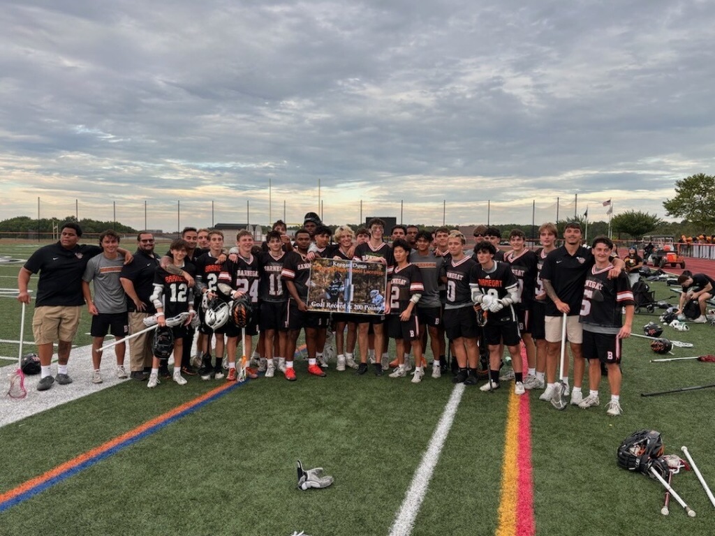 Image of Keegan posing with his lacrosse coaches and team on the field holding a large plaque for his new school record. 