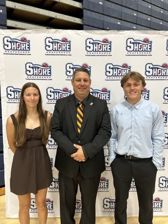 Image of Rachel and Jack posing with the Athletic Director in front of a Shore Conference backdrop. 