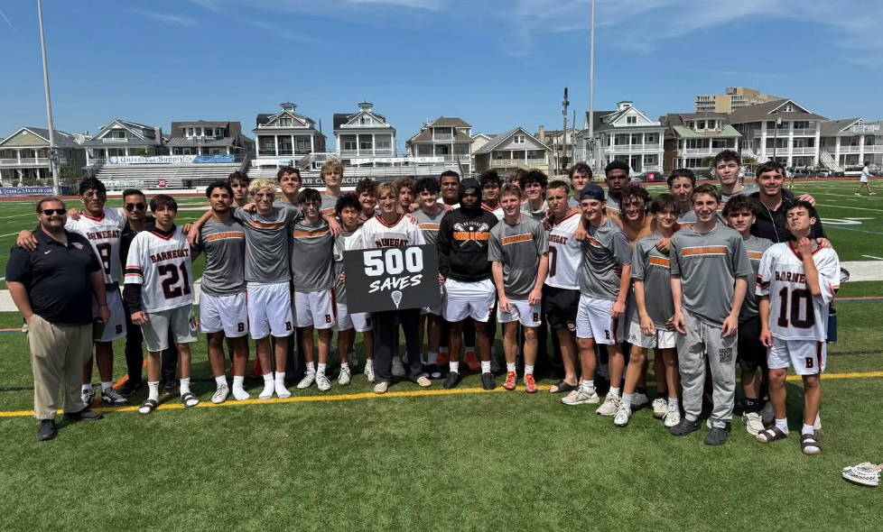 Image of DJ surrounded by the boys lacrosse team and coaches holding a sign in support of his 500th career save. 