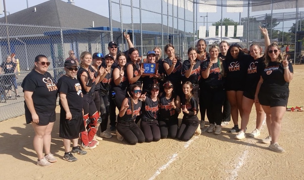 Image of the girls softball team posing with the coaches and Athletic Director on the field holding their trophy.  