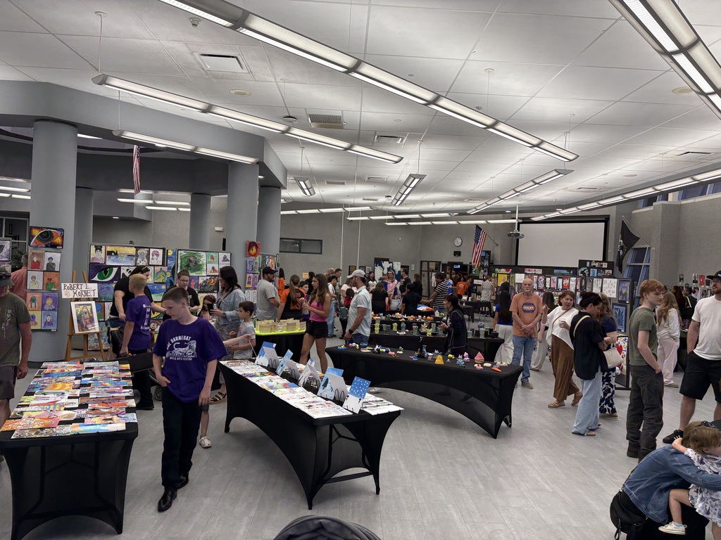 Image of all the artwork on the walls, on tables, and throughout the media center as community members browse the displays. 