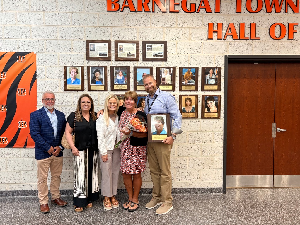 Image of Susan posing in front of the Hall of Fame wall with the Superintendent, Board President, and two staff members. 