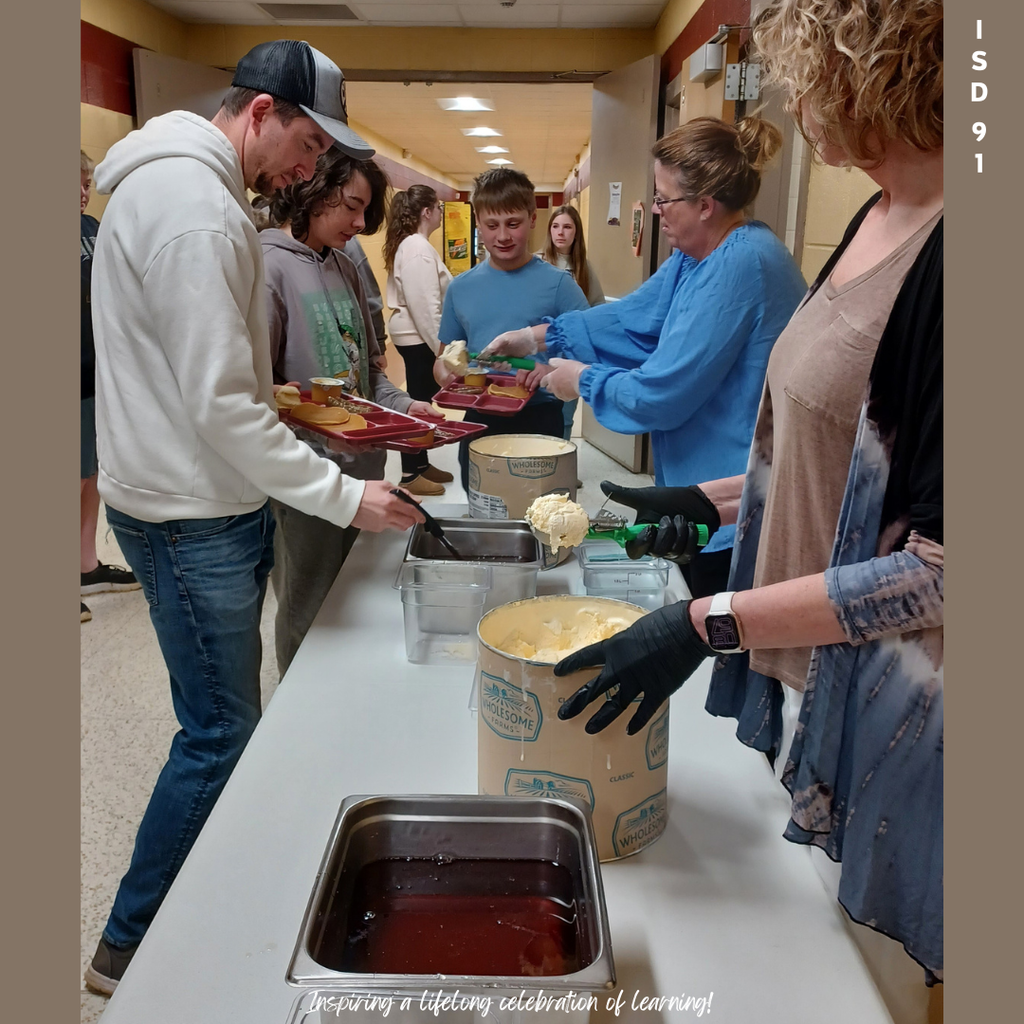 7th graders and parents in line being served pancakes, sausage and ice cream, topped by maple syrup