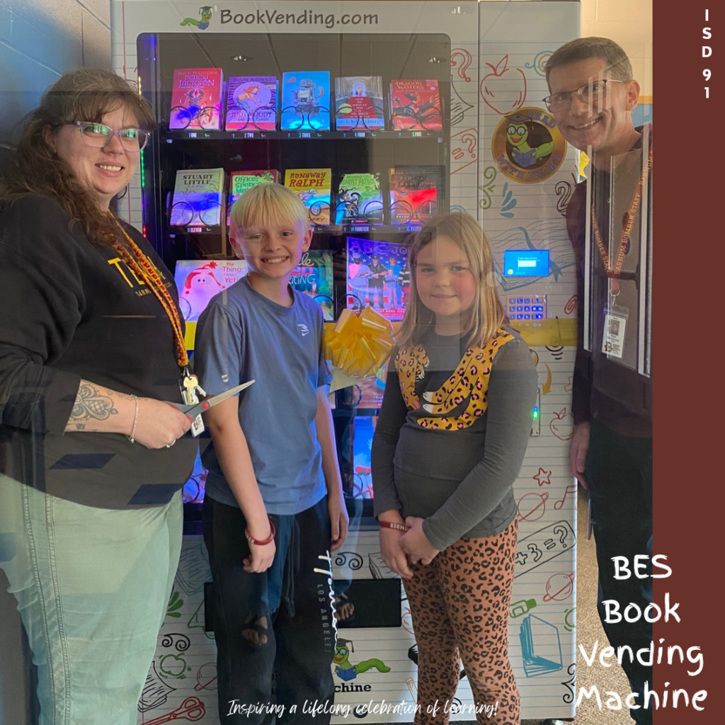 2 staff and 2 students standing in front of a book vending machine with a yellow ribbon tied around it