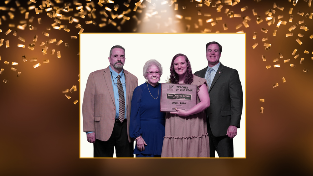 Four people standing together and smiling at the camera. The second person from the right, Kelly Christine McGaha, holds a plaque that reads “Teacher of the Year, Kelly Christine McGaha, 2023–2024.” The background features a celebratory design with golden confetti and a gradient of dark brown to light brown.