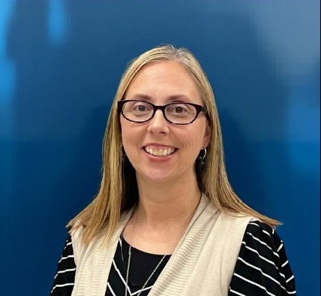 Mrs. Brookshire is smiling at the camera. She is wearing glasses and a black striped blouse with a cream vest.