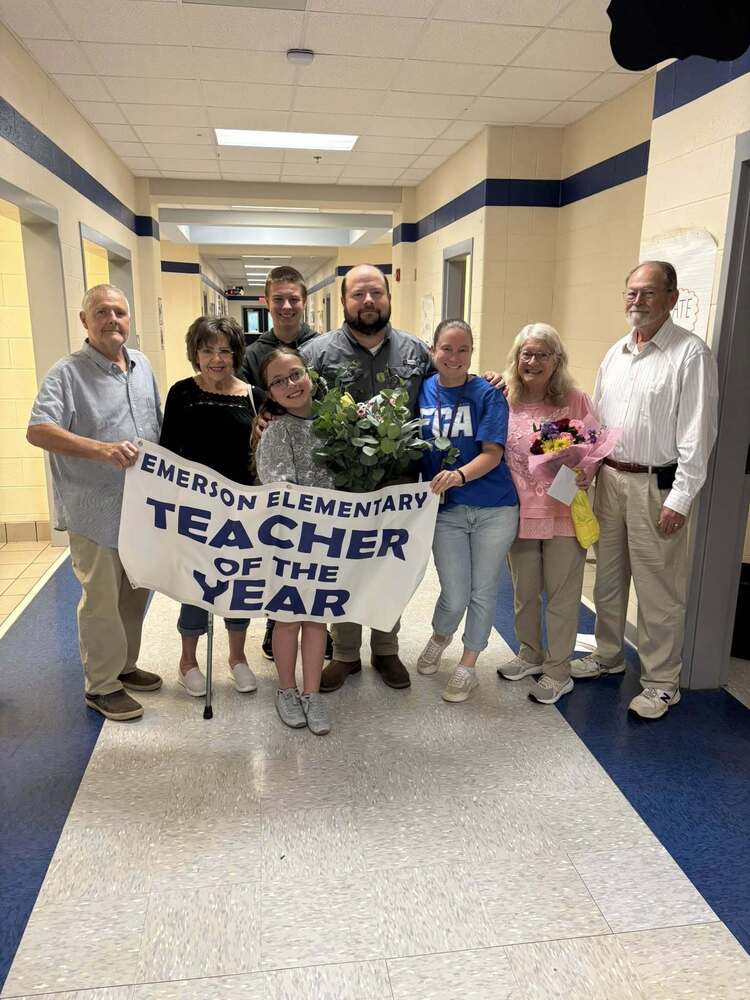 Picture of Mrs. McAllister with her family standing in hall with teacher of the year sign