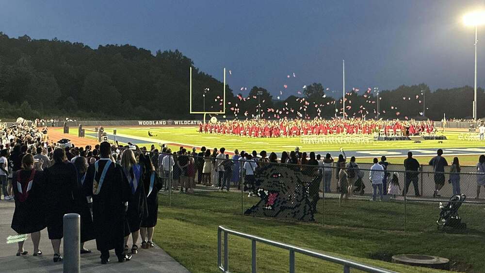 students graduating and throwing their cap in the air inside a football stadium at Woodland High School