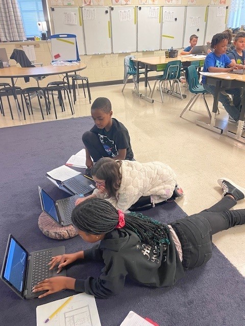 3rd grade students working in a group to research habitats.