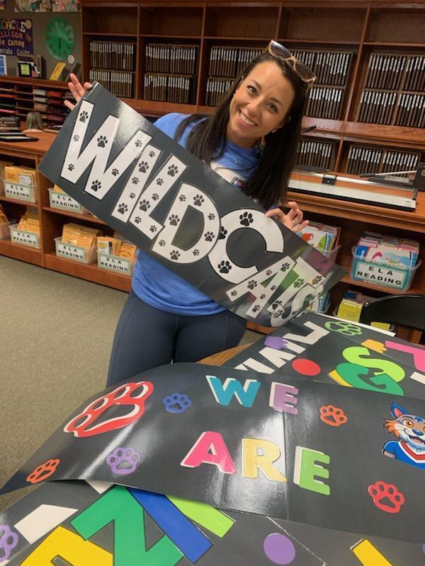 A teacher is holding up a sign that says "Wildcats".