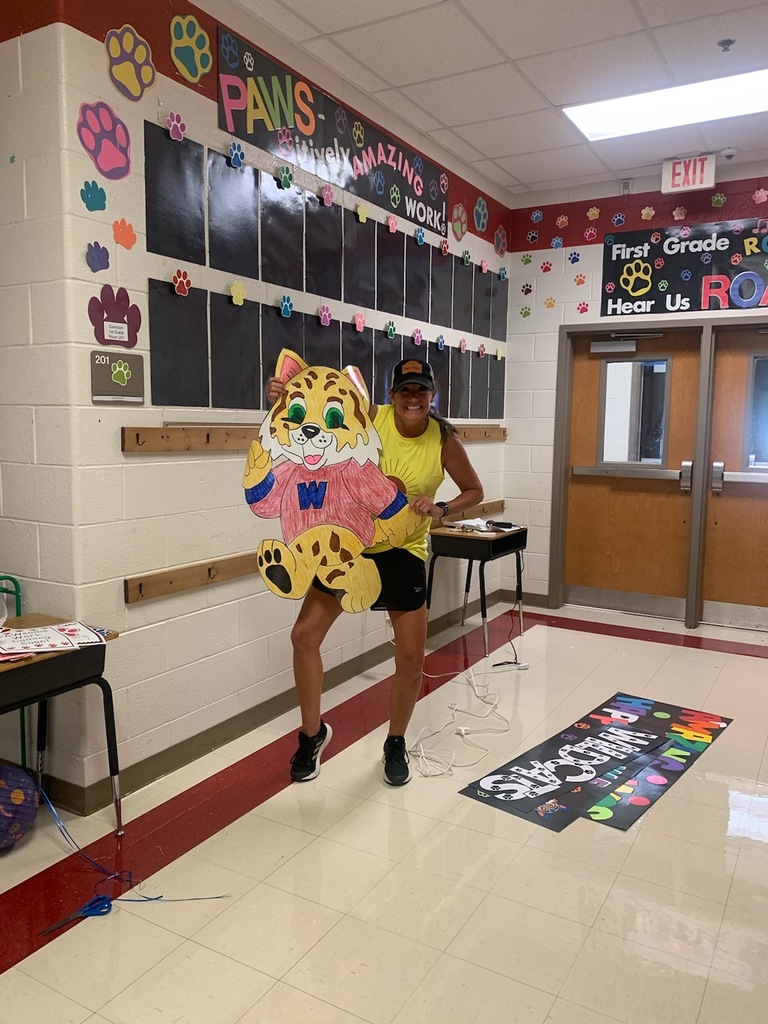 A teacher is in a hallway holding up a wildcat she has made out of posterboard.