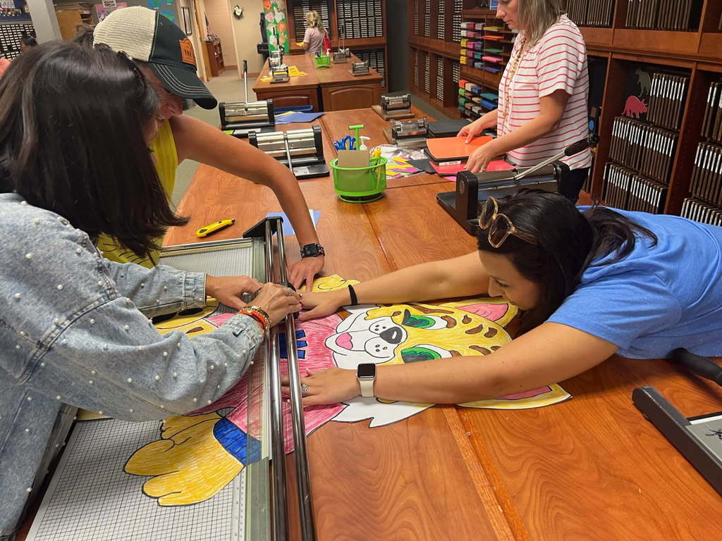 Three teachers are working to cut a wildcat poster with a paper cutter.