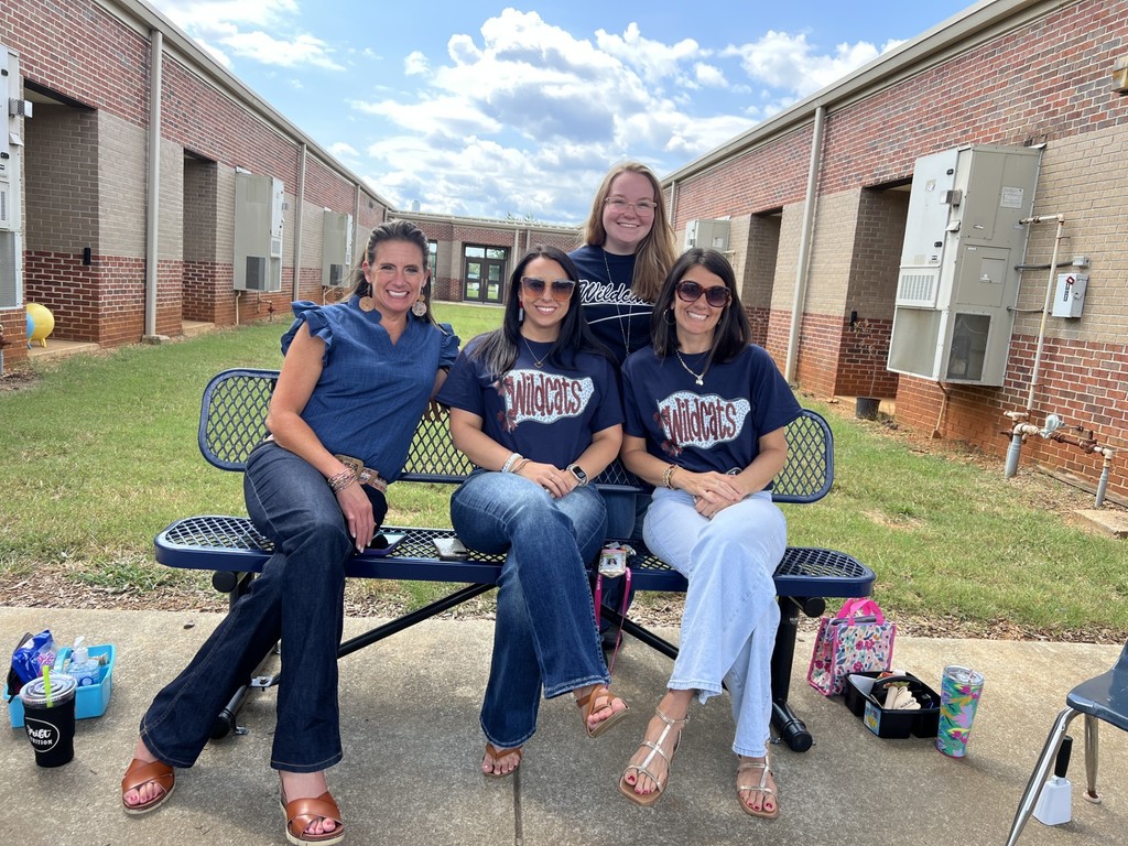 Three teachers are sitting on a bench and one teacher is standing up behind them.  They are all wearing navy shirts.