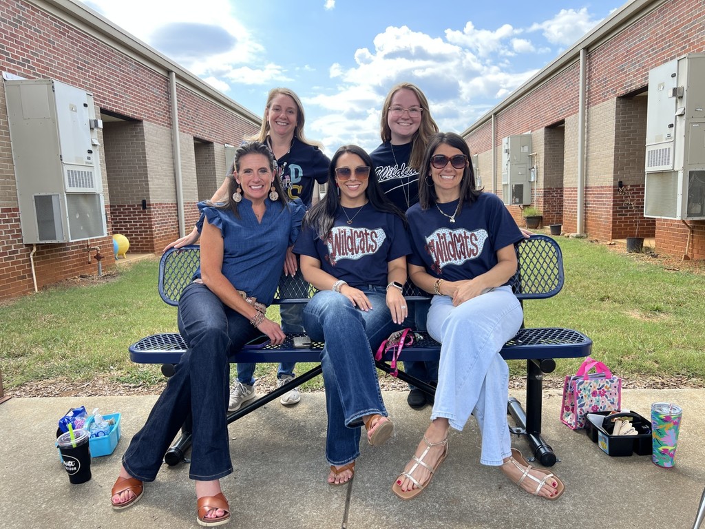 Three teachers are sitting on a bench and two other teachers are standing up behind them.  They are all wearing navy blue shirts.