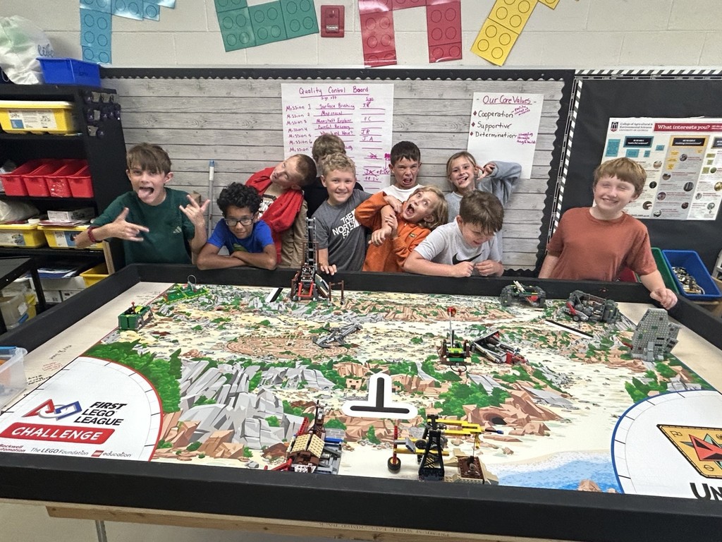 There are ten students standing behind a table with landforms on it and they are making silly faces.  There are nine boys and one girl.