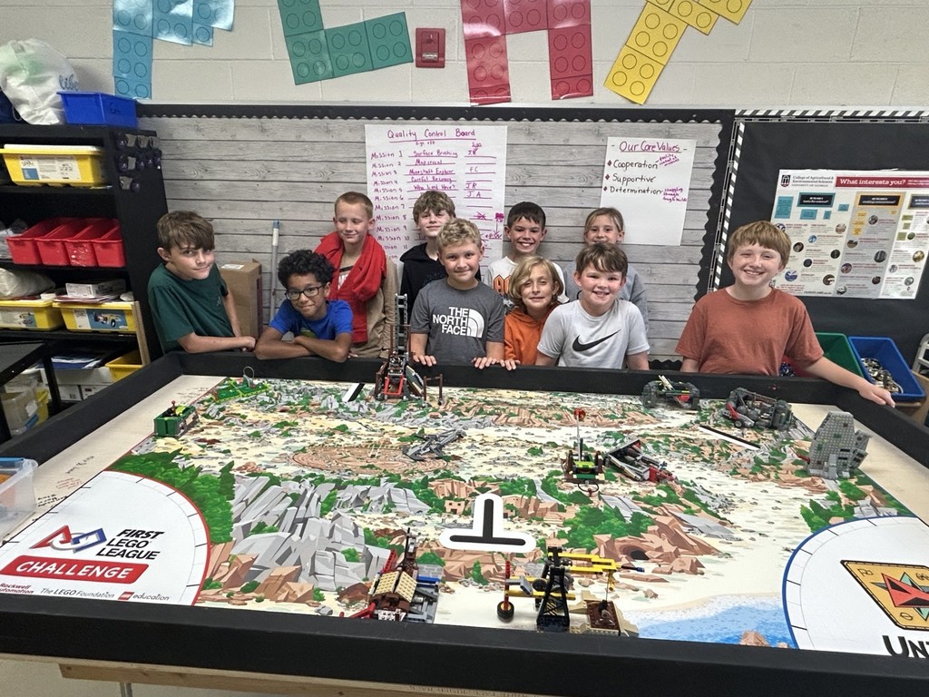 There are ten students (nine boys and one girl) standing behind a Lego table with landforms on it.