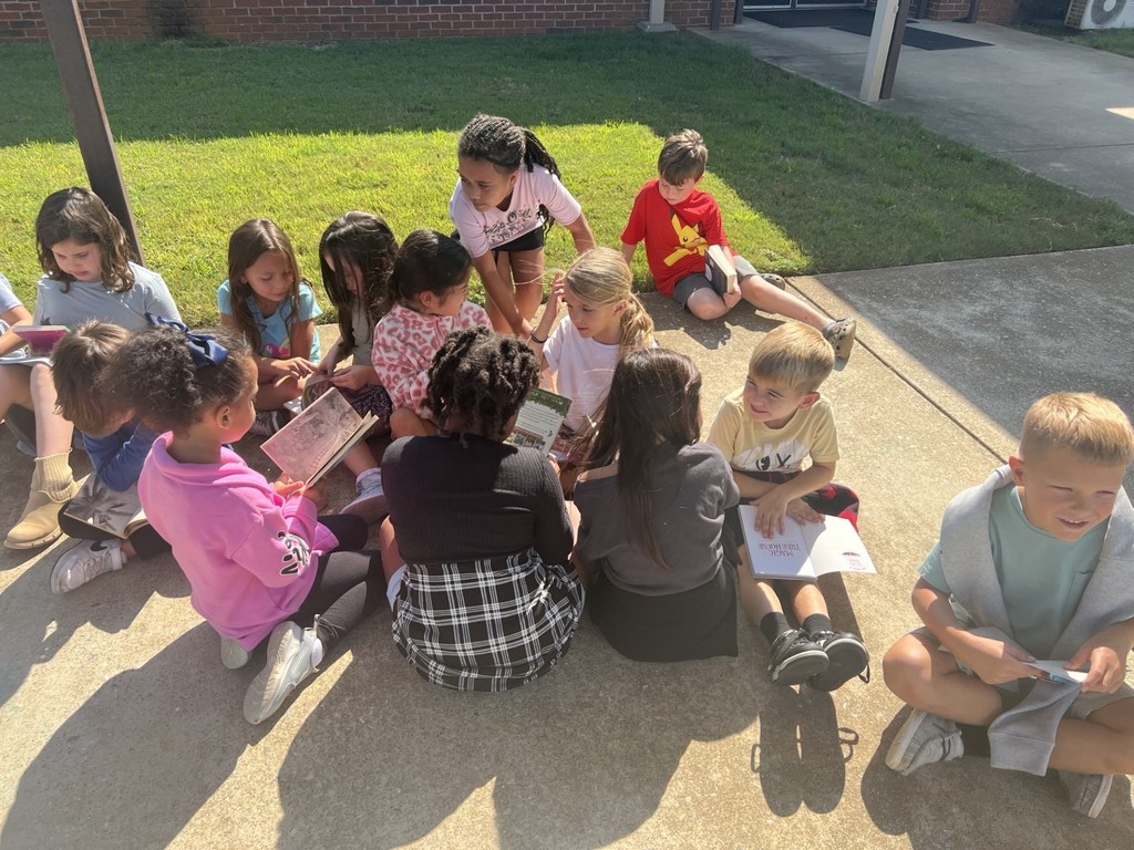 group of students reading books on the sidewalk
