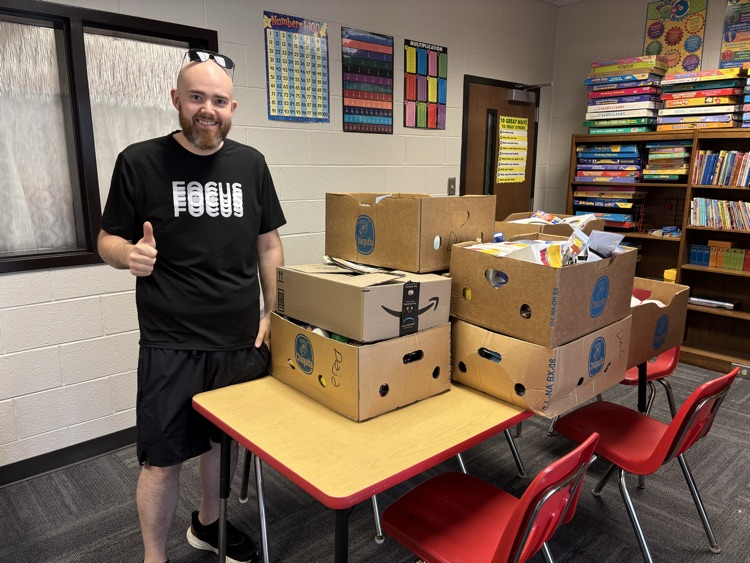 a man with a black shirt on that says “focus” standing in front of boxed that are on a table. the man is holding up his thumb
