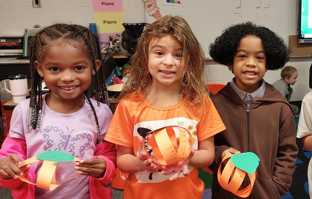Two girls and a boy are holding up the musical pumpkins they made.