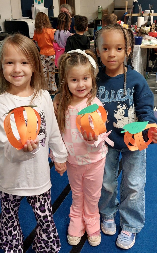 Three girls are holding up the pumpkins they made.