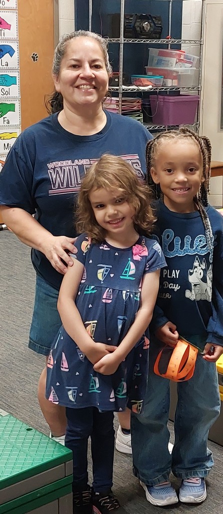 There is a teacher with two girls standing in front of her.  They are all wearing navy.