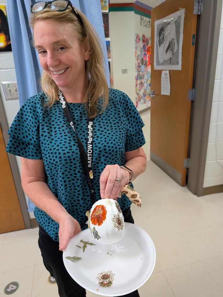 A teacher in a blue shirt holding up a pumpkin she decorated.