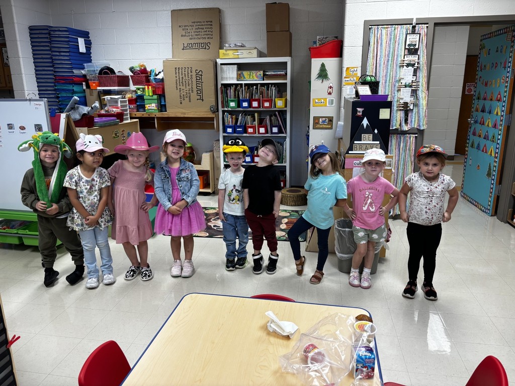 nine students are standing side by side in a classroom with their hats on
