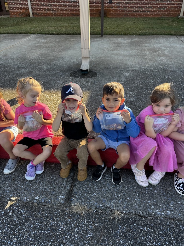 students holding up bags of items they found on the ground outside