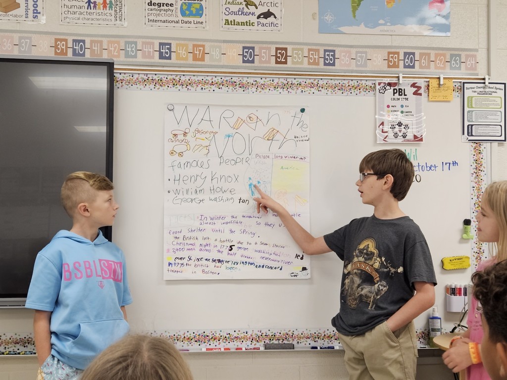 two boys and one girl talking about their project hanging on the board
