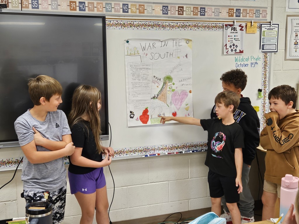 four boys and one girl standing in front of their project at the front of the room in front of the board