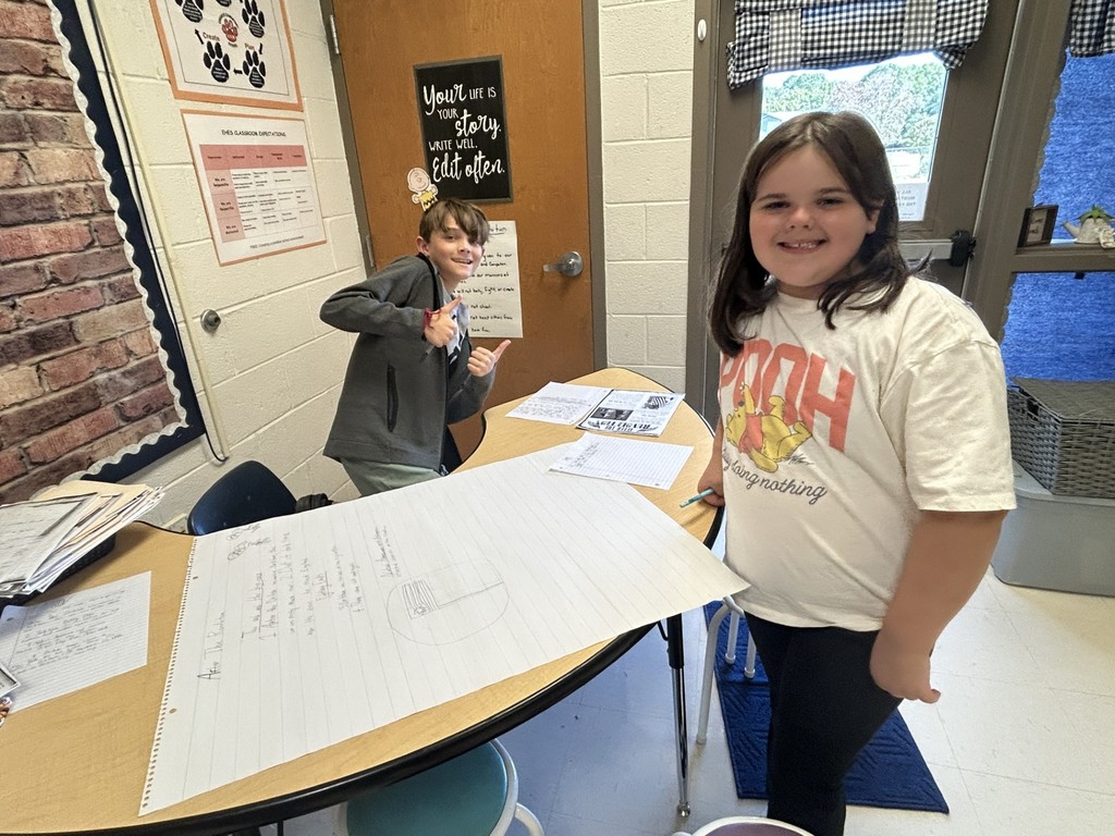 two students standing at a table with chart paper in front of them