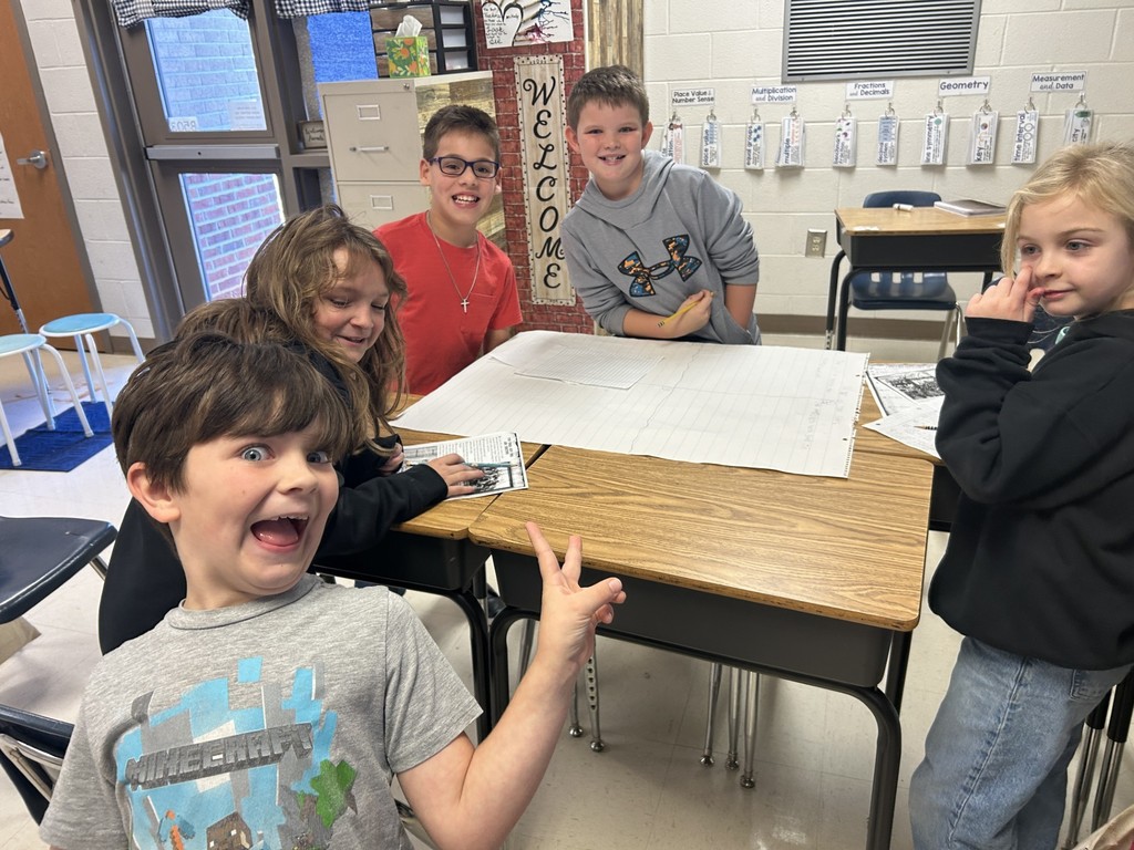 three boys and one girl standing around a desk with chart paper on the desk
