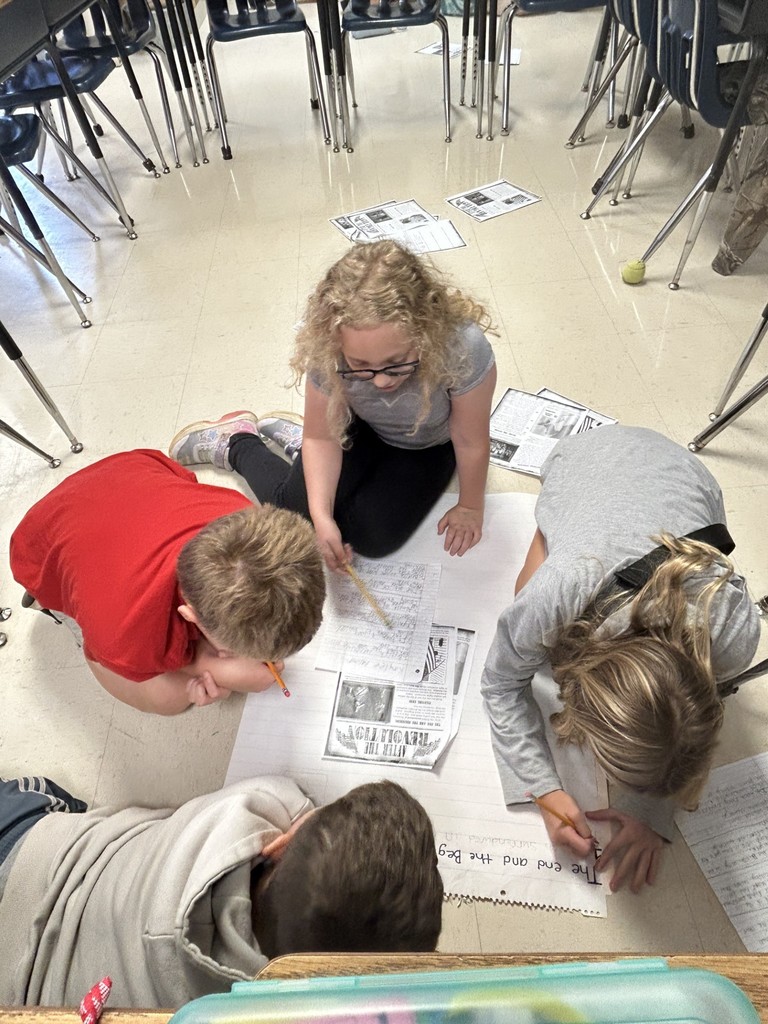 two girls and two boys writing on chart paper on the floor