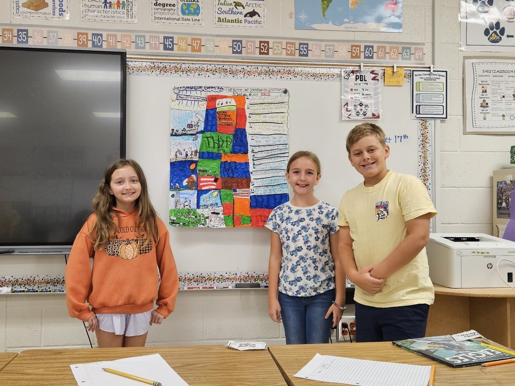 two girls and one boy standing in front of their project on chart paper in front of the board