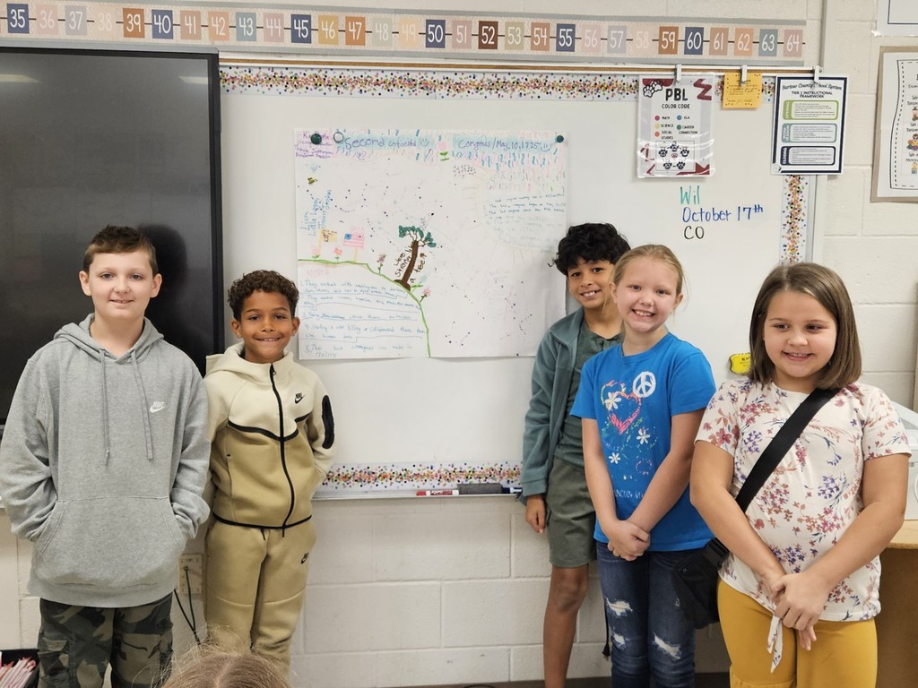 three boys and one girl standing in front of their project hanging on the board