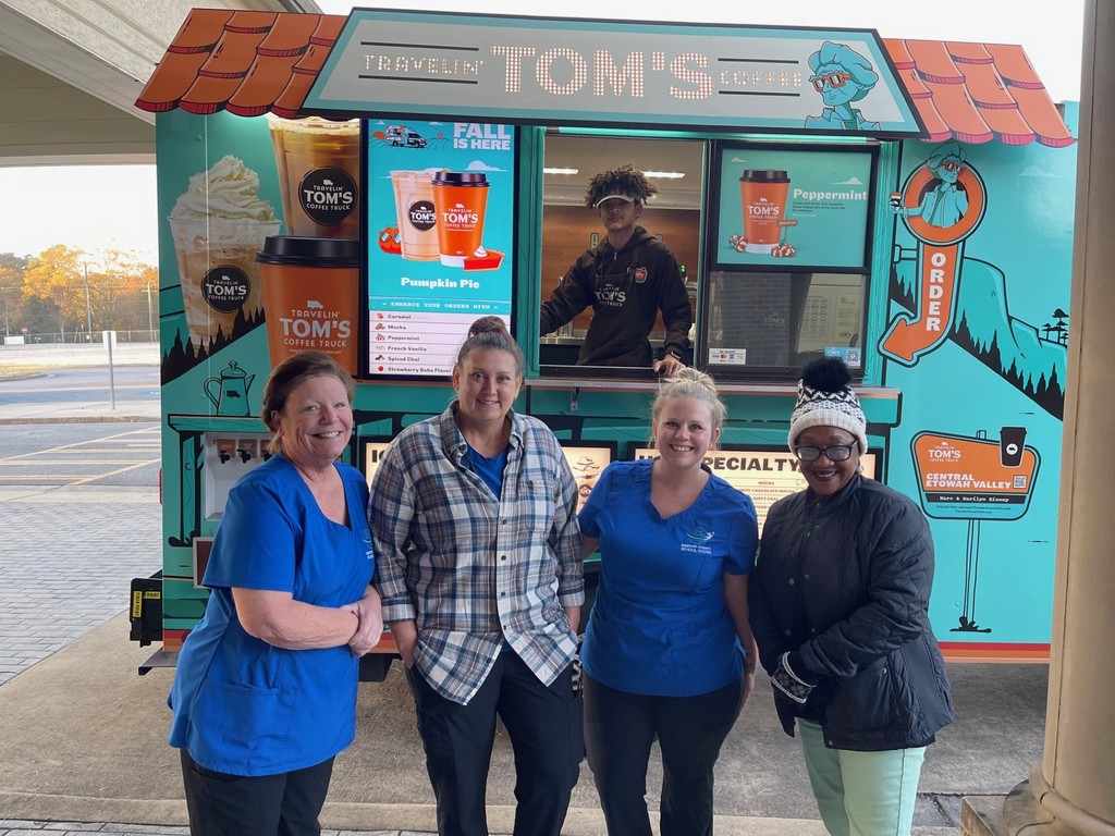 Four female staff members smiling in front of the Tom's coffee truck