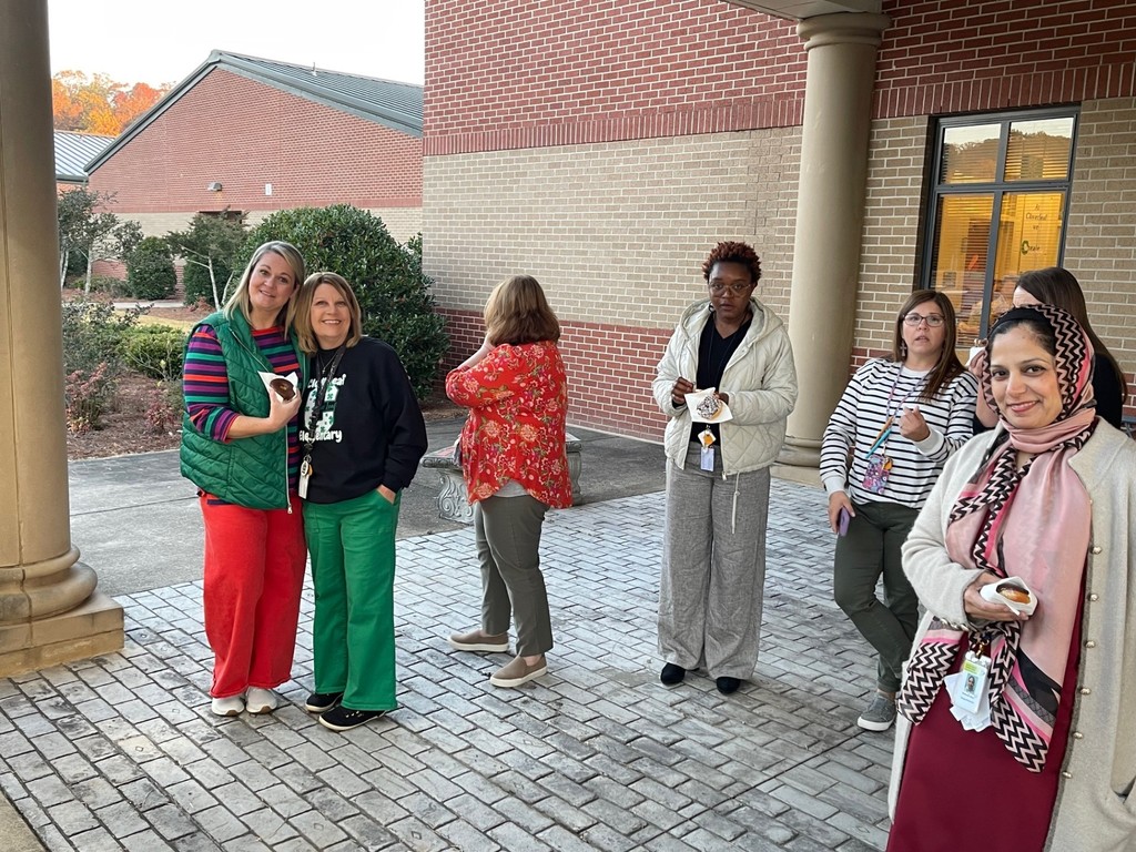 A group of female school employees standing, talking, or smiling while waiting for coffee