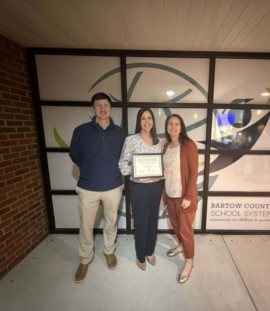 2 women and a man standing in front of a window holding an award. 