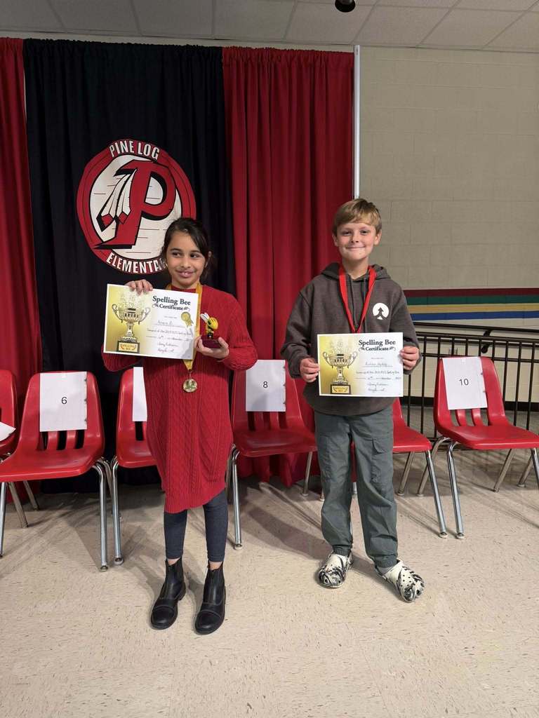 2 students standing in front of red chairs holding an award 