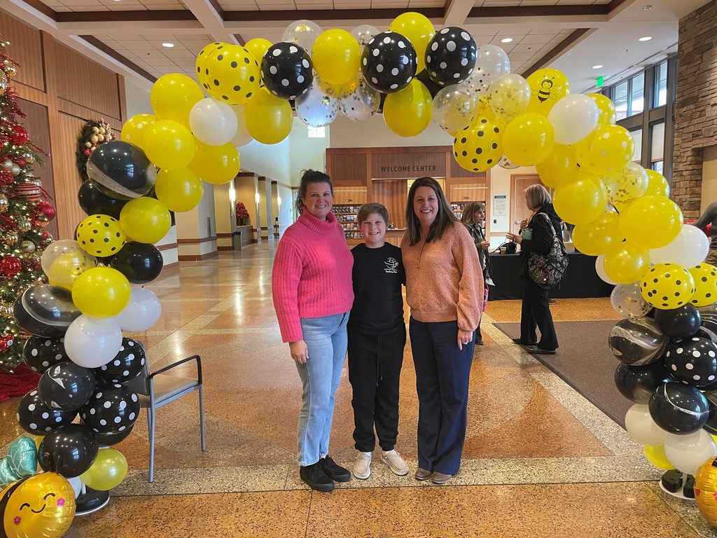 student with parent and principal under balloon arch at spelling bee