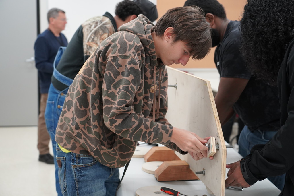 high school student completing a class project with wood, nuts, and bolts