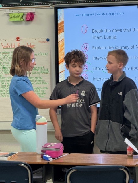 Two boys and one girl are having a debate in front of the class.