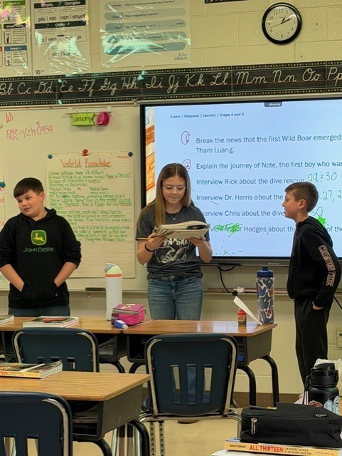 Two boys and one girl are standing in front of a classroom talking.